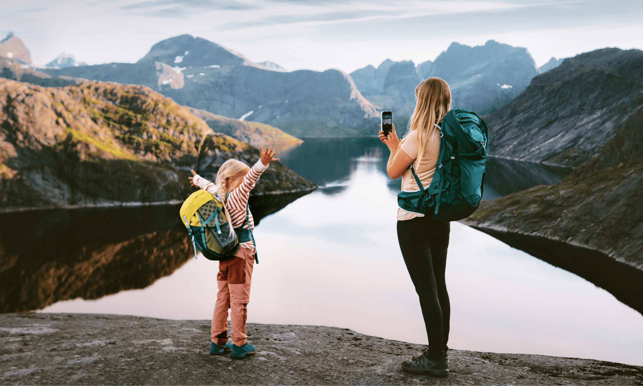 A woman and young girl at an alpine lake taking pictures