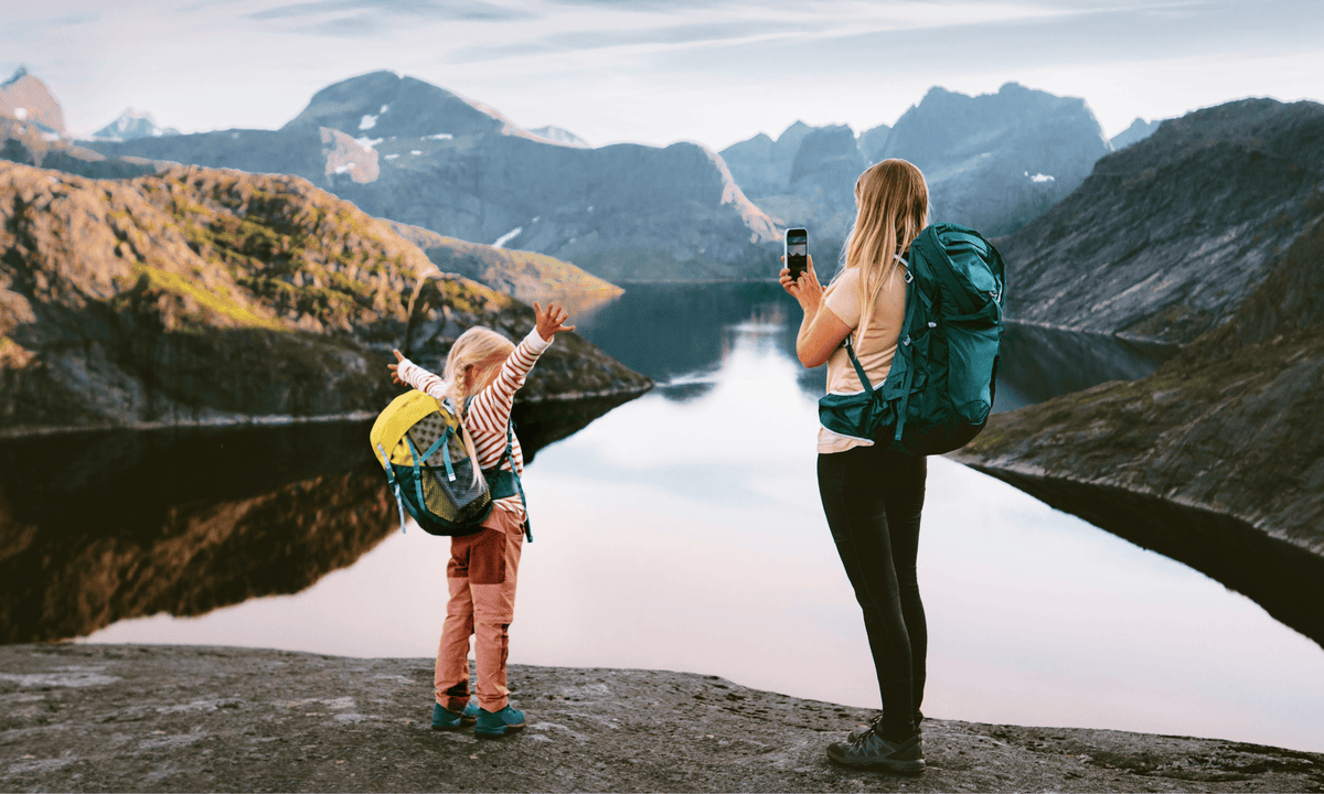 A woman and young girl at an alpine lake taking pictures
