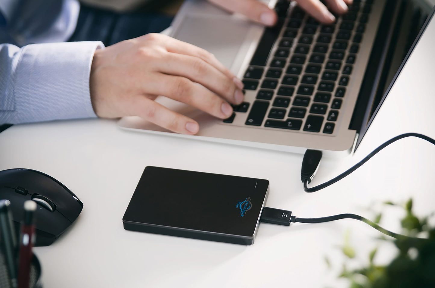 ThePhotoStick Plus plugged into USB port on a laptop and man typing on laptop